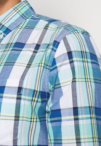 Geruit overhemd met lichtblauwe, turquoise en groene tinten met donkerdere accenten. Knop-down kraag en borstzakdetail. Katoenen stof.