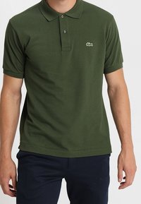 Mörkgrön pikétröja i bomull, med krage, tre knappslå och liten broderad logga på vänster bröst.