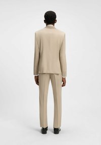 Beige jakkesæt med struktureret blazer og lige bukser. Glat stof, enkelt bagventil, og sorte sko fuldender outfittet.