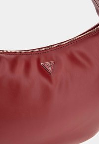 Punane valenaha õlakott sileda tekstuuriga, millel on hõbedane kolmnurkne logo ja kuldne lukustus üleval.