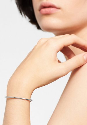 Zilveren bangles met een dun, glad ontwerp, rustend op een hand met lichte huid. Minimalistisch en elegant in stijl.