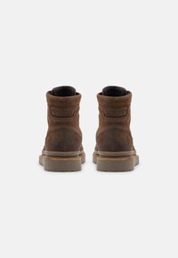 Botine din suede maro, cu guler ridicat la glezne, talpă plată și detalii de cusătură subtile pe margine.