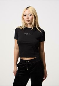 Juoda trumpa marškinėlė, pagaminta iš lygaus audinio, su balta "Juicy Couture SPORT" logo krūtinėje. Trumpi rankovės ir prigludęs dizainas.