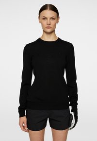 Svart stickad pullover med långa ärmar och rundad halsringning. Ribbad manschett och nederkant. Slät yta, minimalistisk märkning på bröstet. Avslappnad passform.