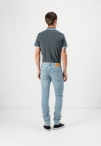 Menns grå polo med hvit kant, kombinert med lyseblå slim-fit jeans og svarte sneakers. Merkelig lærpatch bak på jeansene.