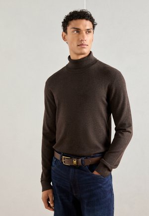 Brun turtleneck genser med en myk tekstur, tettsittende design og lange ermer. Kombinert med blå denimjeans og et brunt belte med spenne i metall.
