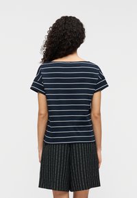 Μπλούζα με κοντά μανίκια σε ναυτικό μπλε χρώμα με ρίγες, φαρδιά λαιμόκοψη και άνετη φόρμα, συνδυασμένη με μαύρη σορτς με λεπτές ρίγες.