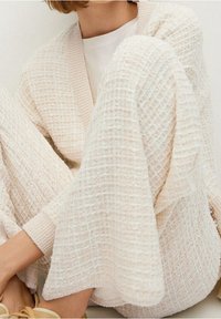 Gebreid vest in off-white met een gestructureerd ruitpatroon, voorzien van een diepe V-hals en brede mouwen, gecombineerd met bijpassende gestructureerde broek.