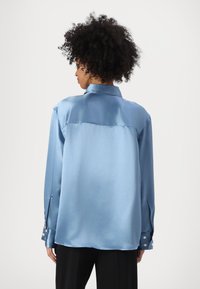 Camicia di raso azzurro chiaro con colletto, maniche lunghe e dettagli a bottoni sui polsini. Tessuto liscio con una vestibilità comoda.