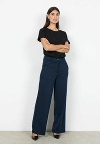 Marineblauwe broek met wijde pijpen van gladde stof, voorzien van een tailleband en zakken, gecombineerd met een aansluitend zwart T-shirt en zwarte hakken.