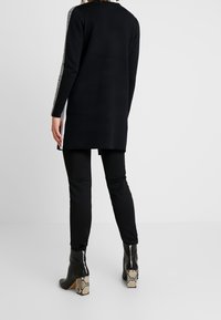 Jersey negro de manga larga con corte recto, con acentos de panel de punto a lo largo de las mangas, combinado con pantalones negros y botas de tacón con estampado de serpiente.