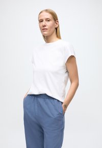 Vit bomulls-T-shirt med rund hals och korta ärmar, kombinerad med löst sittande blå byxor. Tyget ser mjukt och avslappnat ut.