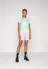 Heled rohelise tie-dye mustriga T-särk, lühikeste varrukatega; roosad lühikesed püksid elastse vööga; mustad sokid ja kingad täiendavad riietust.