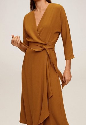 Kietaisumekko sinapinkeltaisena, pehmeästä kankaasta, siinä on V-kaula-aukko, 3/4-hihat, sivusolmittava vyö ja laskeutuva, epäsymmetrinen helma.