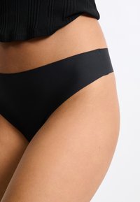 Slip bikini neri con un design senza cuciture, texture liscia e un taglio minimalista, che mettono in risalto una vestibilità comoda attorno alla vita.