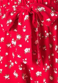 Tejido rojo con un estampado floral que presenta flores blancas. Incluye un detalle de lazo en la cintura. Textura suave, material ligero.