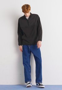 Svart zip-up genser med høy krage, kombinert med løse blå denimjeans og svart-hvite sneakers. Glatt tekstur.