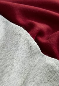 Warstwy bawełnianego materiału w jasnoszarym i ciemnoczerwonym kolorze, charakteryzujące się miękką teksturą oraz subtelnymi różnicami w kolorze i wzorze tkania.