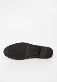 Semelle d'une chaussure habillée en cuir marron avec talon et avant-pied en caoutchouc noir texturé, avec le nom de la marque ALDO embossé près de la voûte plantaire.