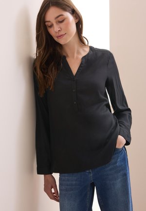 Zwarte blouse met lange mouwen, V-hals, knoopdetails, een soepele textuur en een relaxte pasvorm, gecombineerd met blauwe spijkerbroeken.