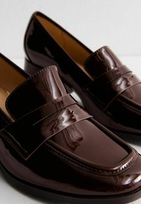 Mocasines de charol marrón con un diseño elegante, que cuentan con una correa en el empeine y un acabado suave y brillante.