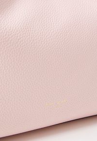 Lichtroze leren tas met een gestructureerd oppervlak. Voorzien van een goudkleurig, geperst "kate spade NEW YORK" logo. Eenvoudig, rechthoekig ontwerp.