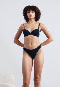 Sutien din material moi, cu burete, de culoare bleumarin, cu bretele ajustabile, însoțit de un bikini cu talie înaltă, ambele fiind realizate dintr-un material elastic și neted. Design minimalist.