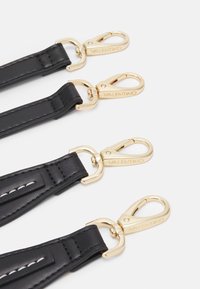 Schwarze Lederbänder mit goldenen Metallverschlüssen, die mit gravierten Marken und kontrastierenden weißen Nähten versehen sind, angeordnet in parallelen Reihen.