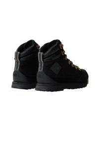 Bottines de randonnée noires en matériaux de daim et cuir, avec des œillets dorés bien visibles, un col rembourré et une semelle en caoutchouc texturée. Comprend un détail de logo embossé.