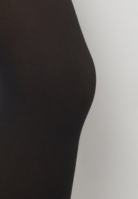 Opake schwarze Strumpfhosen mit glatter Textur, die eine Nahaufnahme des Beinbereichs zeigen, einschließlich eines figurbetonten Designs und leichtem Glanz.