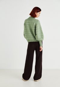 Pull en tricot vert clair avec un col montant et des manches bouffantes, associé à un pantalon large noir mettant en valeur une texture côtelée.