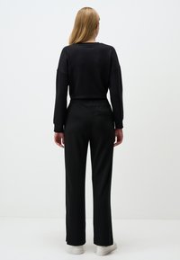 Czarny, długi rękaw, luźny top, połączony z czarnymi spodniami wysokiego stanu z elastycznym pasem i bocznymi rozcięciami. Białe sneakersy.