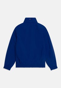 Giacca blu navy con colletto, polsini e orlo elastici. Presenta una delicata cucitura del logo sul colletto. Texture liscia e design leggero.