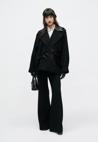 Čierna nadrozmerná bunda s koženým golierom a vreckom, so zapínaním v páse. Kombinovaná s čiernymi zvonovými nohavicami a čiernymi doplnkami.