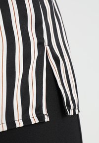 Chemise en tissu rayé avec des rayures audacieuses noires, blanches et brunes ; comprend une fente latérale et une texture lisse.