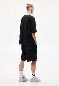 Černé oversized tričko s krátkými rukávy a zničenými detaily, spárované s černými šortkami s kapsami, nošené s světlými teniskami.