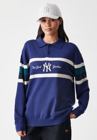 Temno modra pulover z dolgimi rokavi, bele in teal stripe ter izvezenim logotipom "New York Yankees" na sredini. V kombinaciji s svetlo sivo kapo.