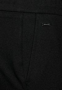 Svarta sportbyxor i slätt tyg, med platt midja, sidoficka och liten märkesetikett på baksidan.