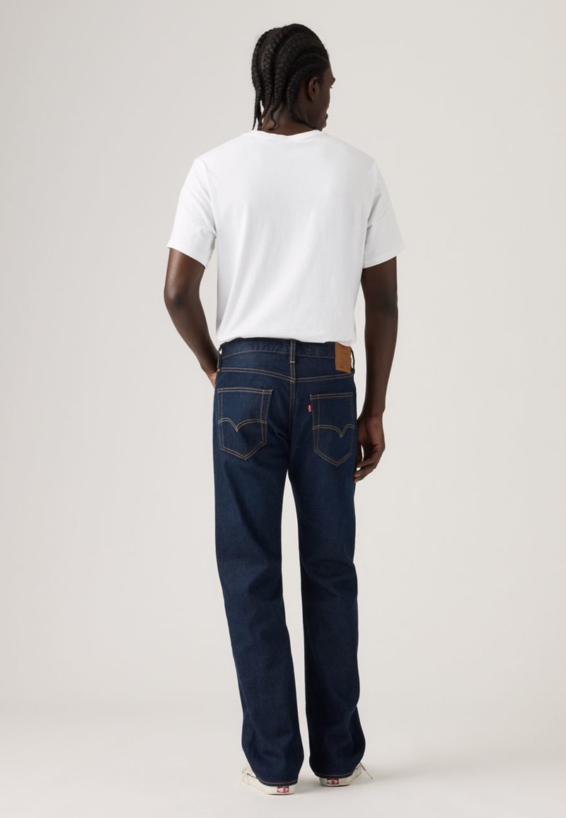 Dark blue denim jeans with a straight leg cut, contrasting yellow stitching, and two back pockets featuring a logo above the right pocket.