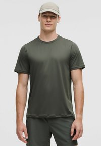 T-shirt de sport vert olive en tissu lisse et évacuant l'humidité, à manches courtes et col rond, porté avec un short assorti.