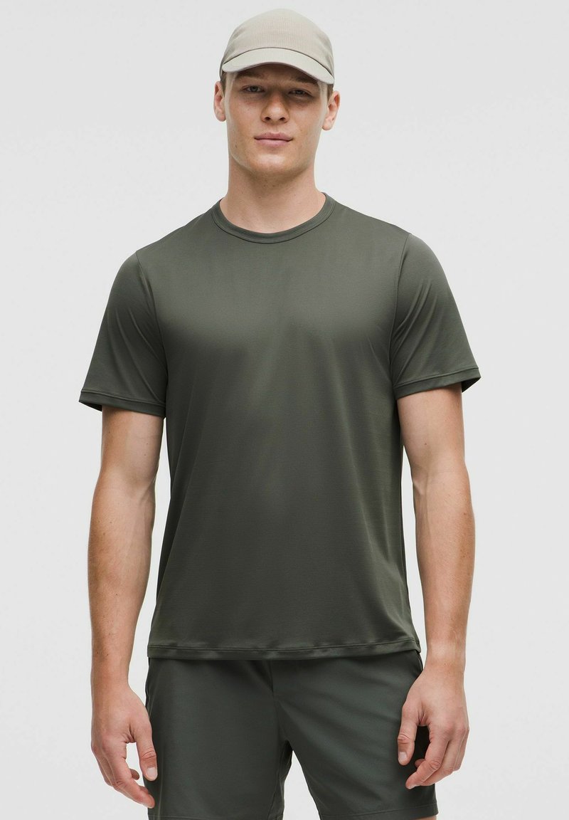 T-shirt de sport vert olive en tissu lisse et évacuant l'humidité, à manches courtes et col rond, porté avec un short assorti.