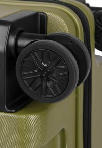 Angolo di una valigia rigida verde con una ruota nera che presenta un design geometrico, una superficie testurizzata e una cerniera resistente.