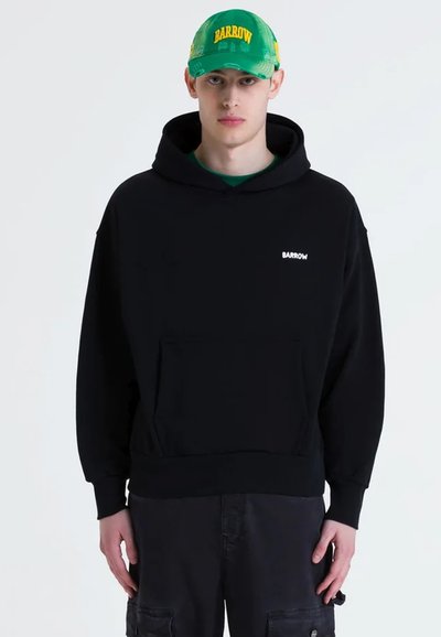Sweatshirt à capuche noire avec une poche avant et le logo blanc "BARROW". Le modèle porte une casquette verte avec du texte jaune et s'accorde avec un pantalon noir.