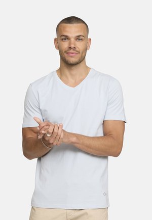 T-shirt bleu clair à manches courtes en V en tissu doux ; arbore un petit logo en forme de diamant en bas à droite ; texture lisse, coupe décontractée.