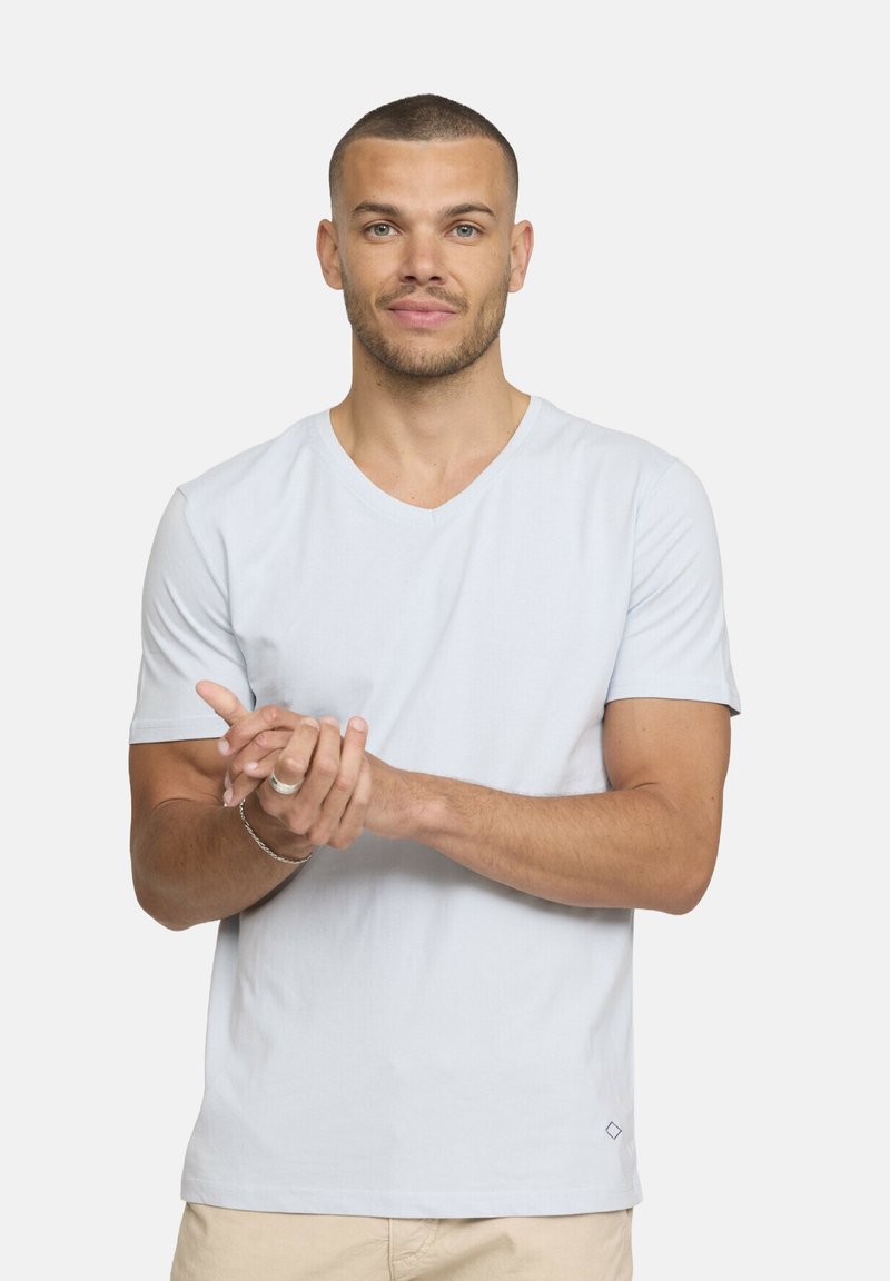 T-shirt bleu clair à manches courtes en V en tissu doux ; arbore un petit logo en forme de diamant en bas à droite ; texture lisse, coupe décontractée.