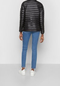 Sort dunjakke med vandrette quiltede linjer, kombineret med blå skinny jeans og hvide platform-sneakers. Fokus på en glat, skinnende finish.