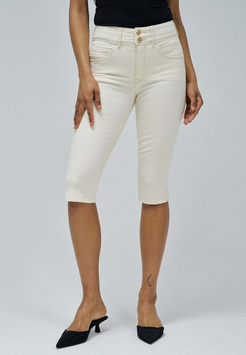 Vaqueros capri de color beige claro con dos botones frontales, trabillas para el cinturón y bolsillos traseros. Textura de denim suave, acabados a la altura de la mitad de la pantorrilla.
