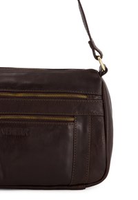 Brun læder crossbody taske med gyldne lynlåse, der har flere lynlåslommer og en tekstureret overflade. Justerbar rem inkluderet.