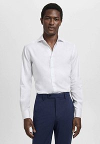 Witte blouse met lange mouwen en een puntkraag, met een knopenfront, gecombineerd met donkerblauwe broek. Glad stof, getailleerde pasvorm, geen zichtbare patronen.