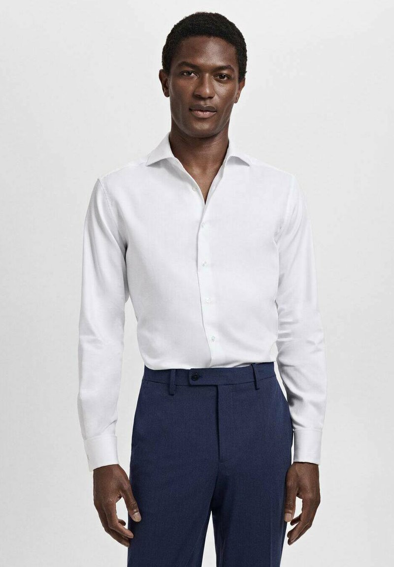 Witte blouse met lange mouwen en een puntkraag, met een knopenfront, gecombineerd met donkerblauwe broek. Glad stof, getailleerde pasvorm, geen zichtbare patronen.